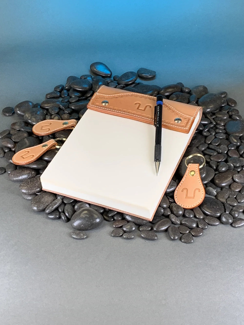 A tooled leather notepad cover with a pen and matching key fobs.