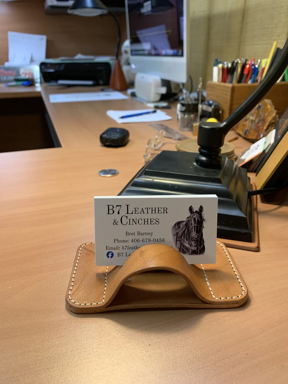 The same leather business card holder in use on a desk, beside a stamping press.