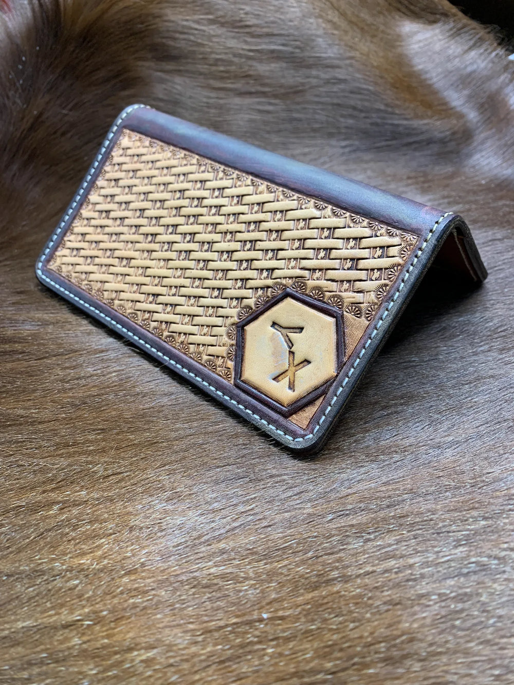 A basketweave-tooled leather checkbook cover with a ranch brand set into a hexagon panel.