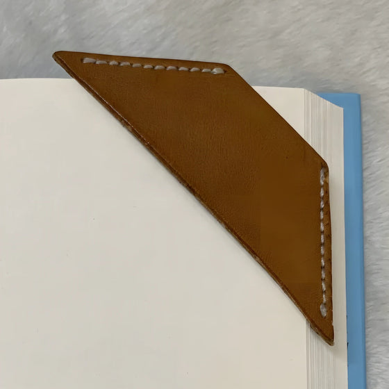 A plain leather corner bookmark, unstamped, slipped over the corner of a page.