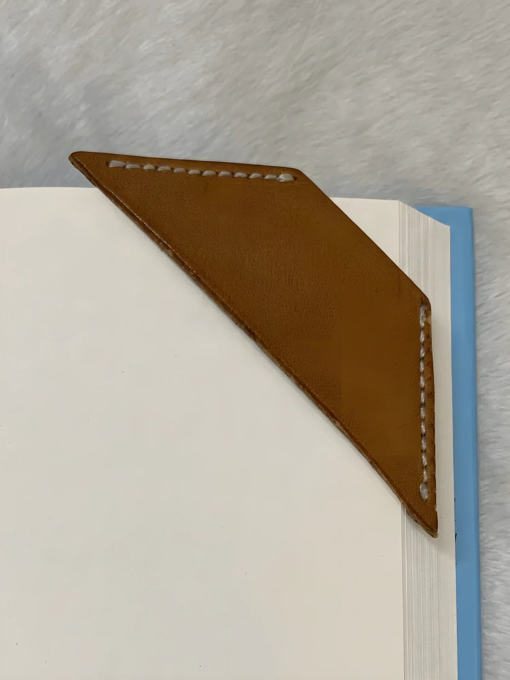 A plain leather corner bookmark, unstamped, slipped over the corner of a page.
