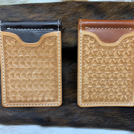Two hand-tooled leather money clip wallets on a brindle cowhide.