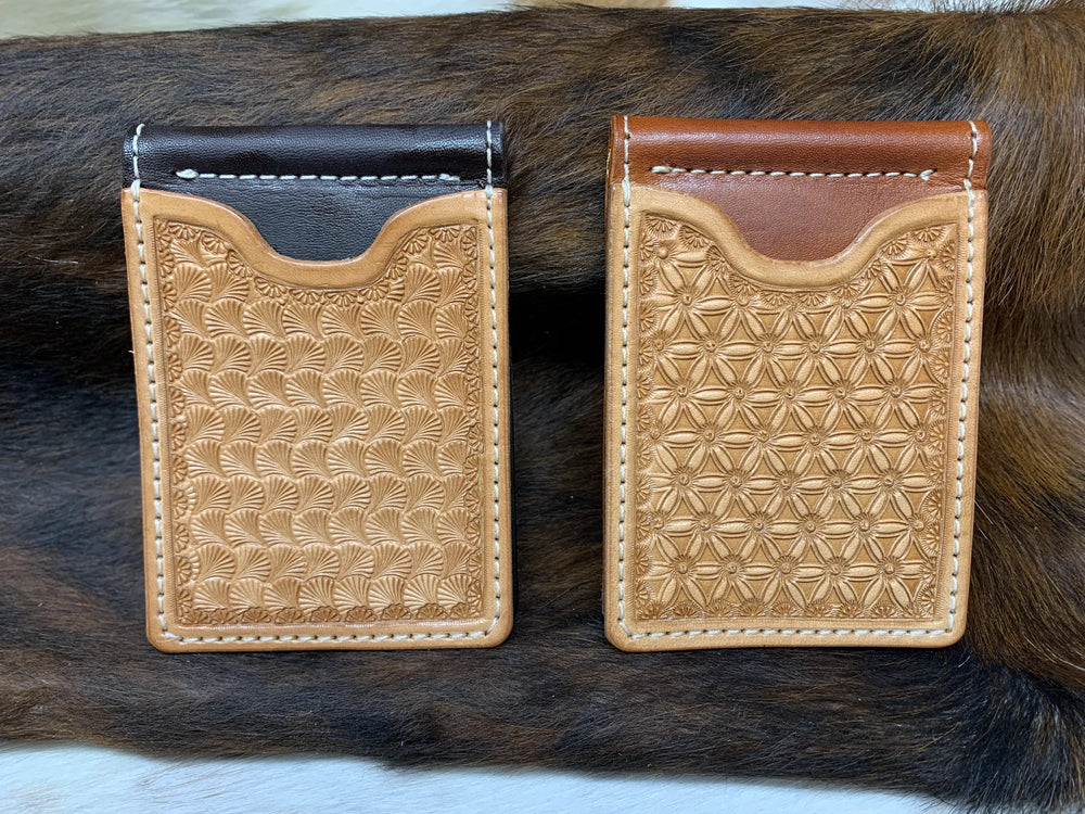 Two hand-tooled leather money clip wallets on a brindle cowhide.