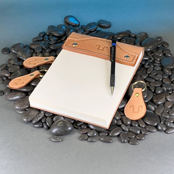 A tooled leather notepad cover with a pen and matching key fobs.