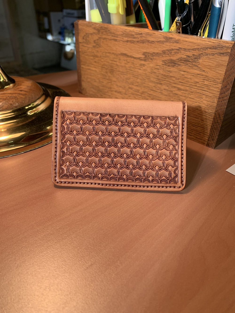 A hand-tooled business card wallet with a geometric stamped panel, standing on a desk.